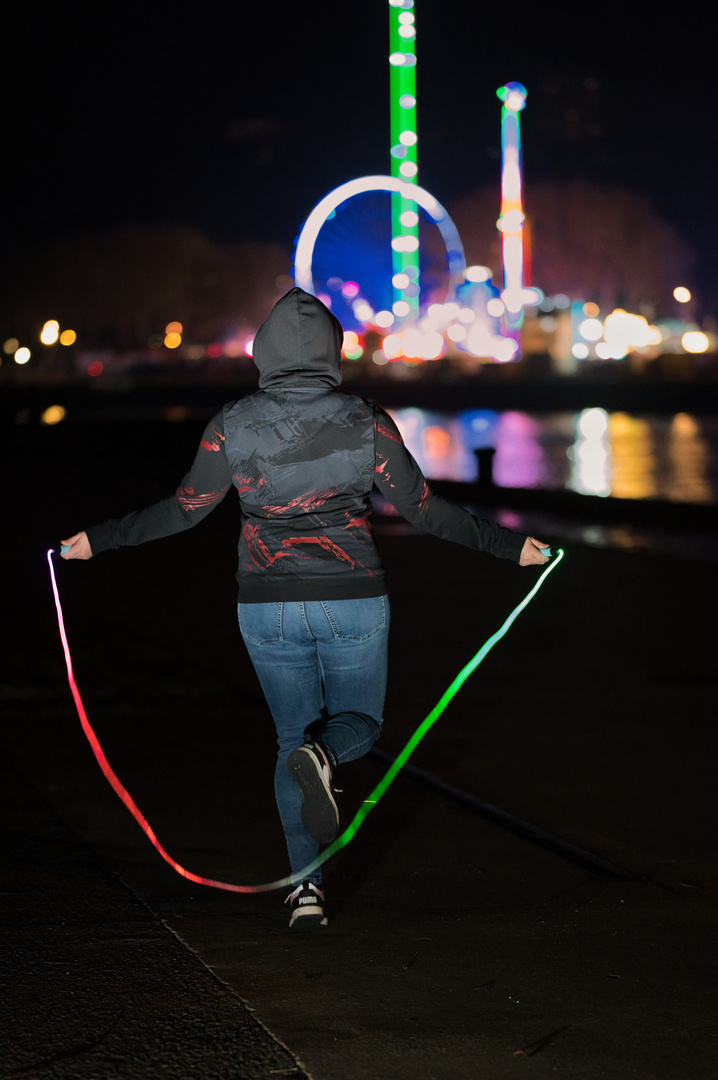 Femme photographiée de dos avec une corde à sauter lumineuse sur les quais de Rouen