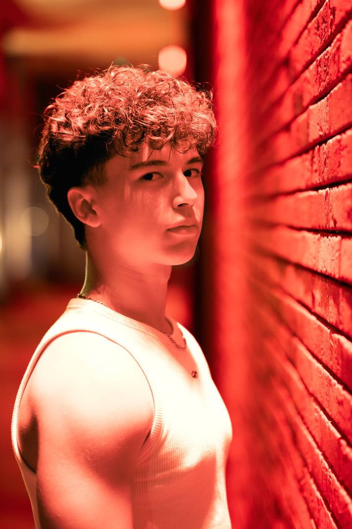 Aurélien près d'un mur en briques sous une lumière rouge